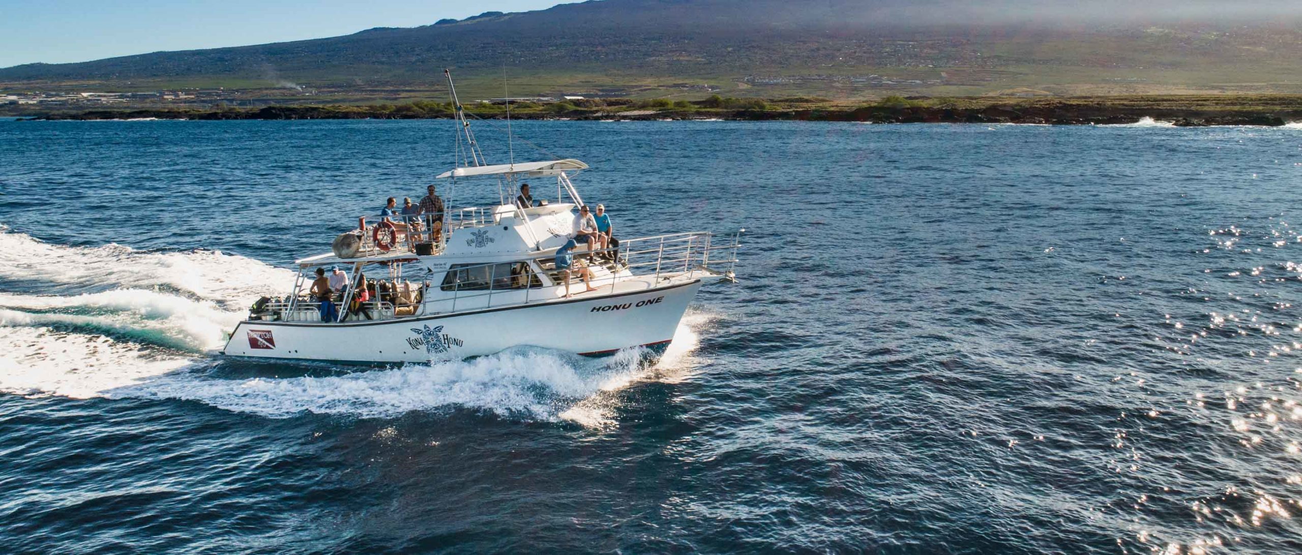 a dive boat cruising along the coast of the big island of hawaii with the island in the background