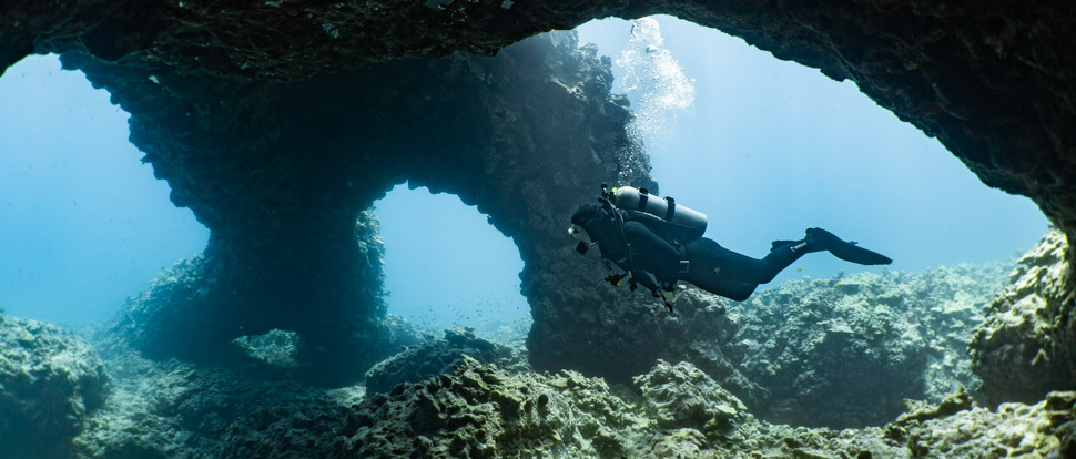 a diver swims through a triple arch with reefs below