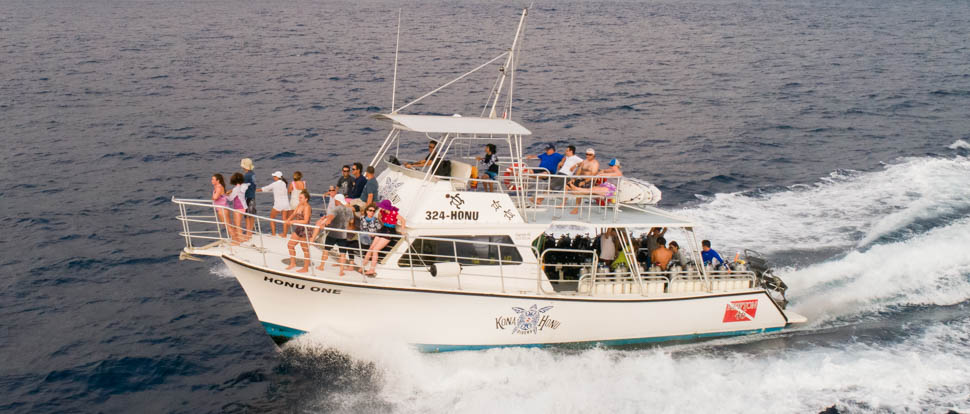 Boat cruising in the ocean with people on board on the bow, top deck and lower deck with scuba tanks on the side