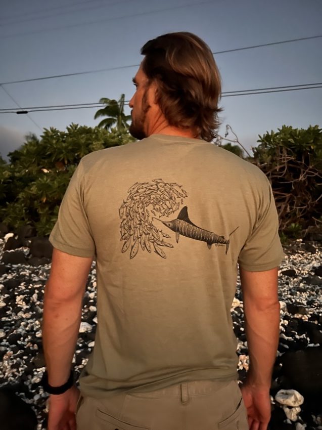 man wearing olive shirt with marlin chasing school of fish on the back