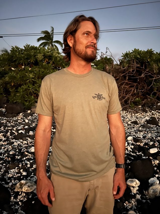 man wearing Kona Honu Divers logo shirt standing on beach