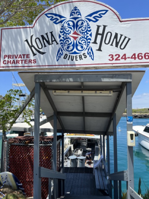 Dive sing with Kona Honu Divers logo and stairs leading down to a dock and a boat backed up to it