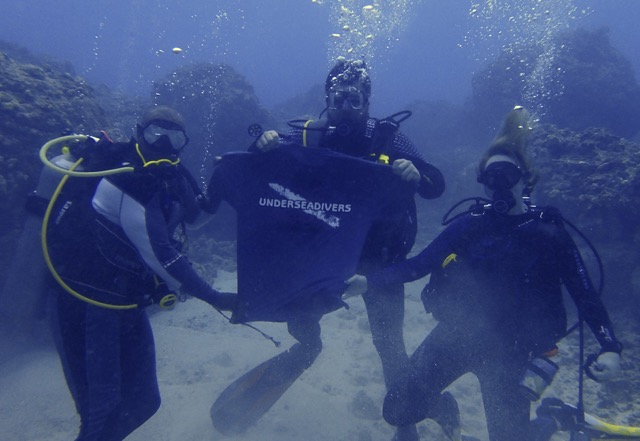 divers pose underwater one holding a t-shirt