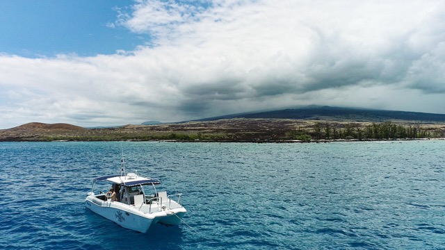 a catamaran dive boat sits in the water near shore of the big island of Hawaii