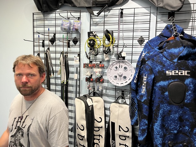 a man stands in front of freediving products inside a dive shop
