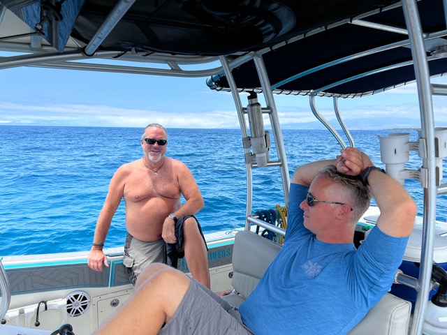 2 men lounge in a boat with ocean behind