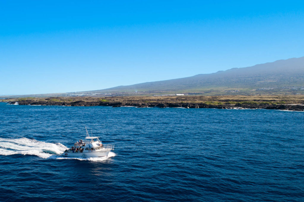 aerial view of a dive boat cruising along the lava rock coast of the big island of hawaii