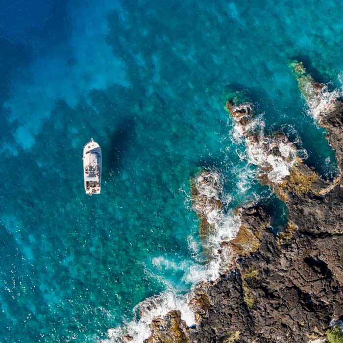 overhead aerial of a dive boat siting in the ocean near a lava rock coast