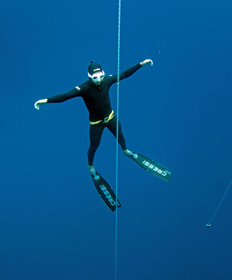 a freediver floating next to a line with arms outstretched to his sides