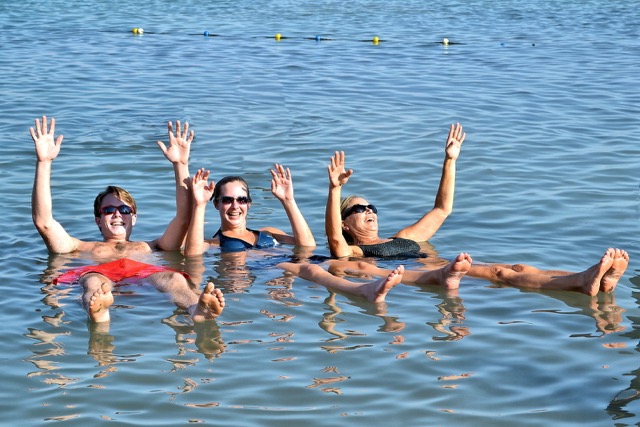a man and two women floating with arms in the air in the Dead Sea