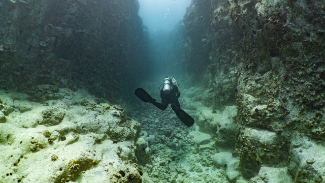 diver swimming underwater in a rocky channel