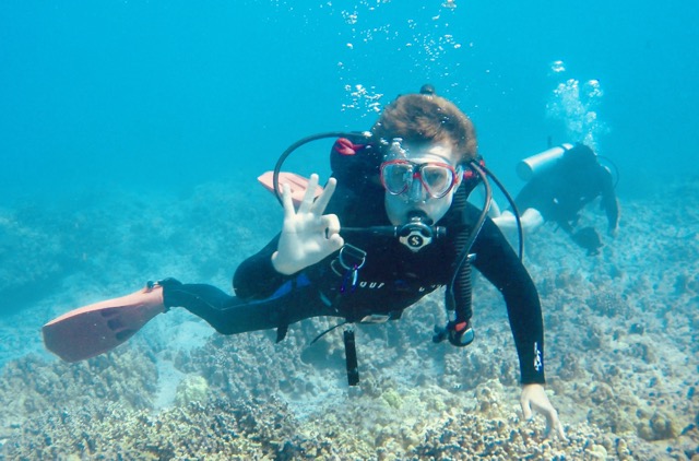 a male diver gives an okay sign with reef behind