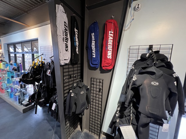 inside of a dive shop are some wetsuits and some fin bags