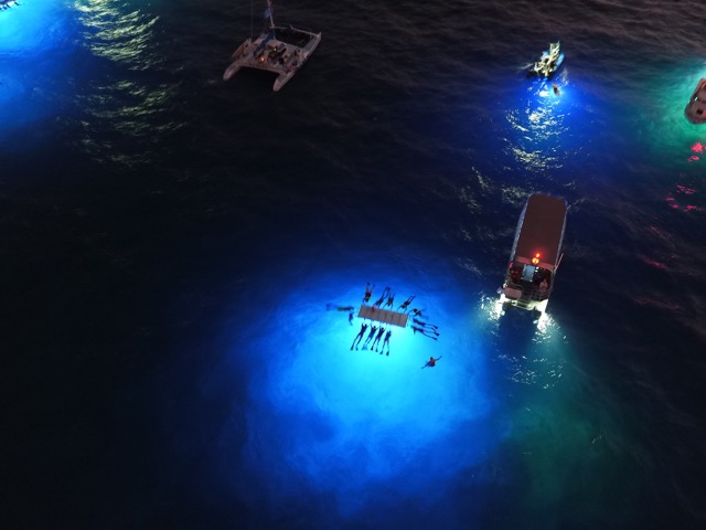 aerial overhead view of the keahou manta site at night with snorkelers and boats on the ocean surface
