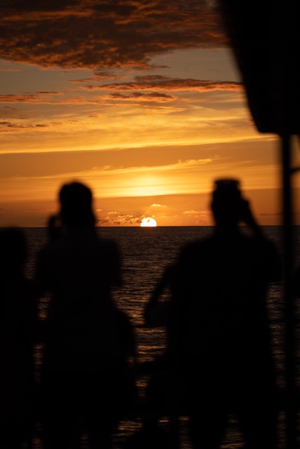 the sun sets over the ocean with peoples silhouettes in the foreground