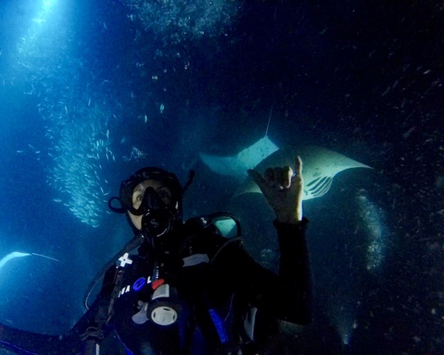 diver at night with manta ray behind