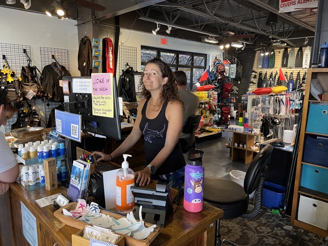 inside a dive shop front desk with a smiling woman behind it
