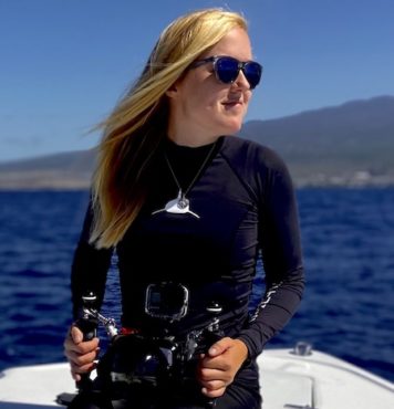 Headshot of Kaitlyn sitting on a boat on the ocean holding a camera in an underwater housing