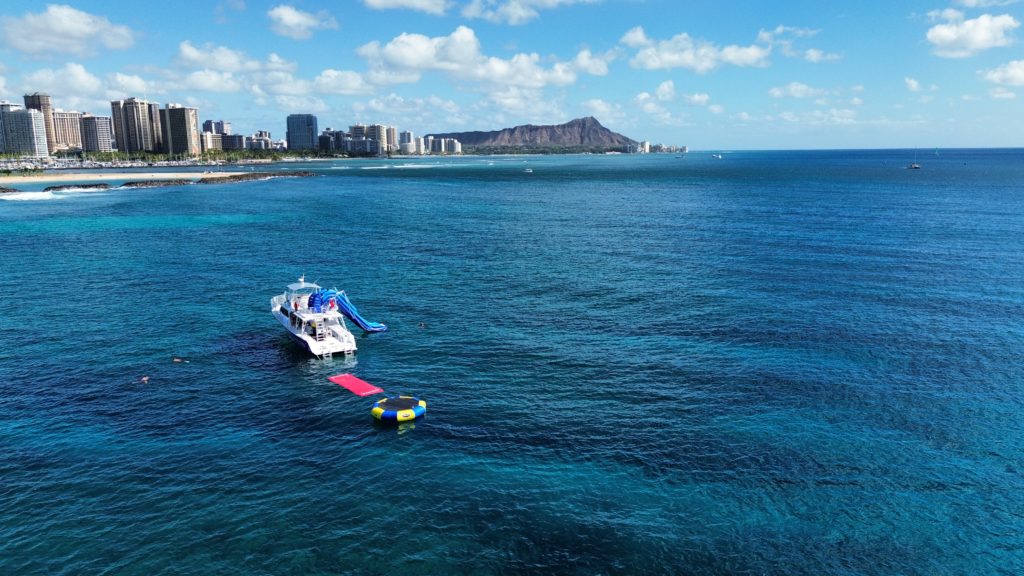 a large boat sits in calm ocean water off the coast of oahu with daimondhead in the background