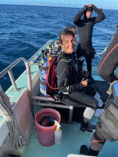 a woman scuba diver sitting on the side of a dive boat and smiling