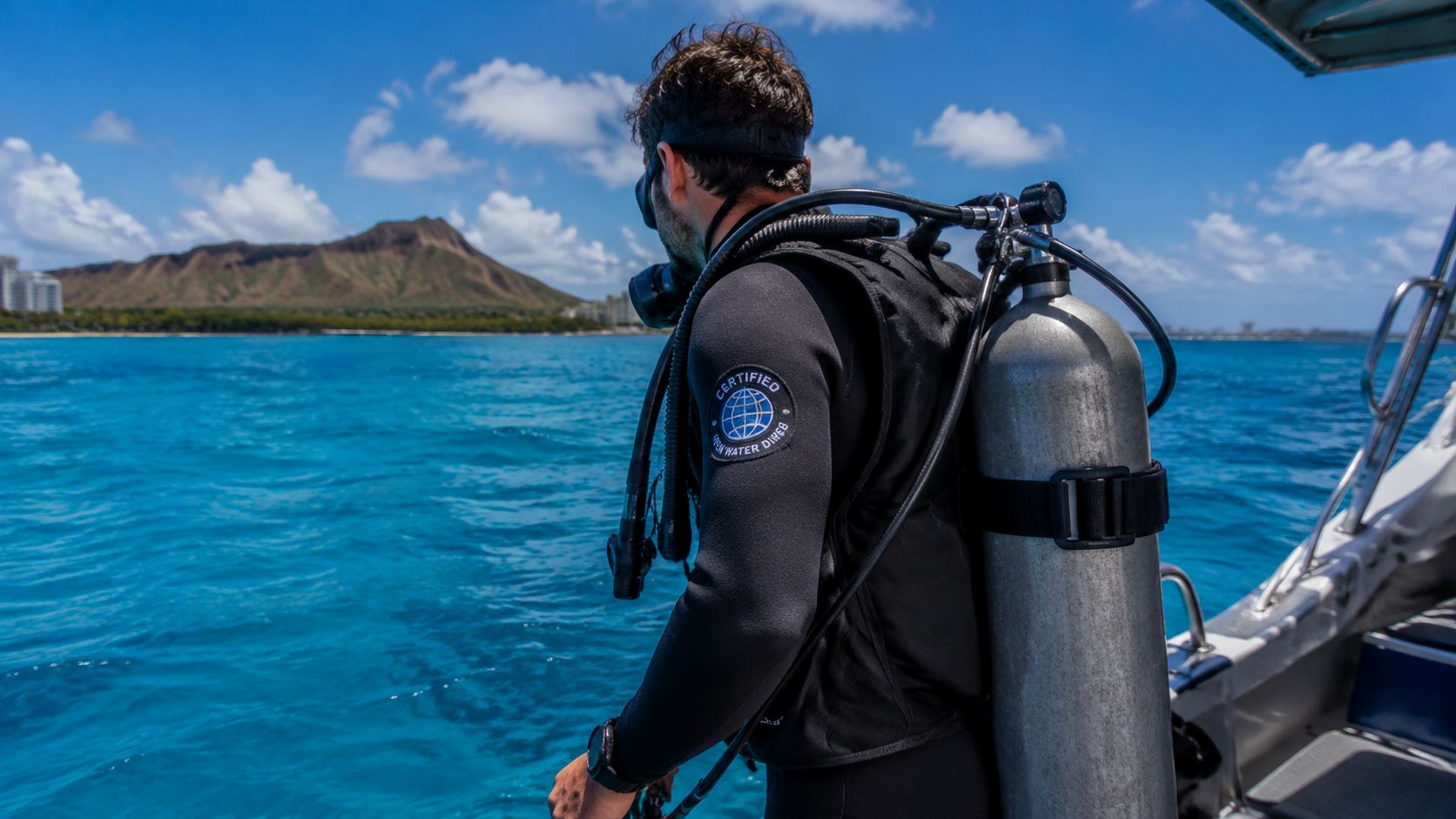 A scuba diver wearing full gear prepares to jump into the clear blue water near Diamond Head, Hawaii.