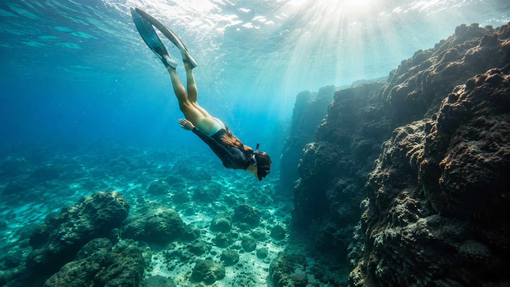 A woman free diving through a clear blue underwater canyon off the coast of Hawaii.