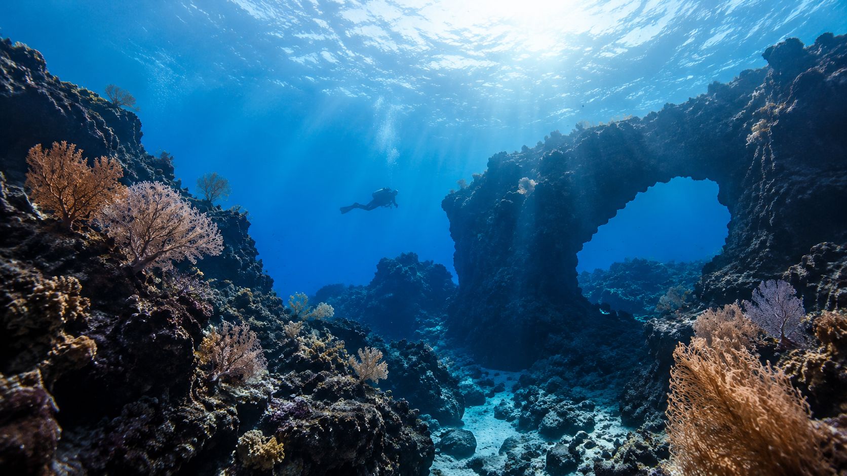A scuba diver explores a stunning underwater volcanic rock arch formation in the crystal clear ocean waters.