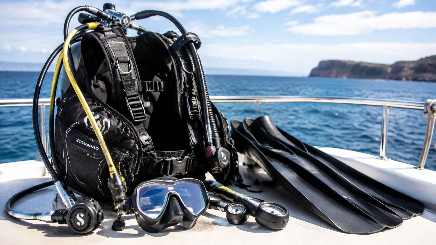 Scuba diving equipment including a black buoyancy compensator, mask, fins, and gauges on a boat deck.