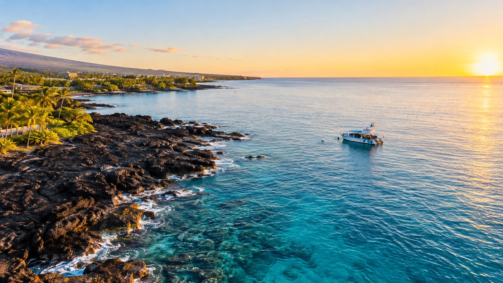 A boat filled with snorkelers floating on crystal clear turquoise water off a rocky volcanic shoreline at sunset.
