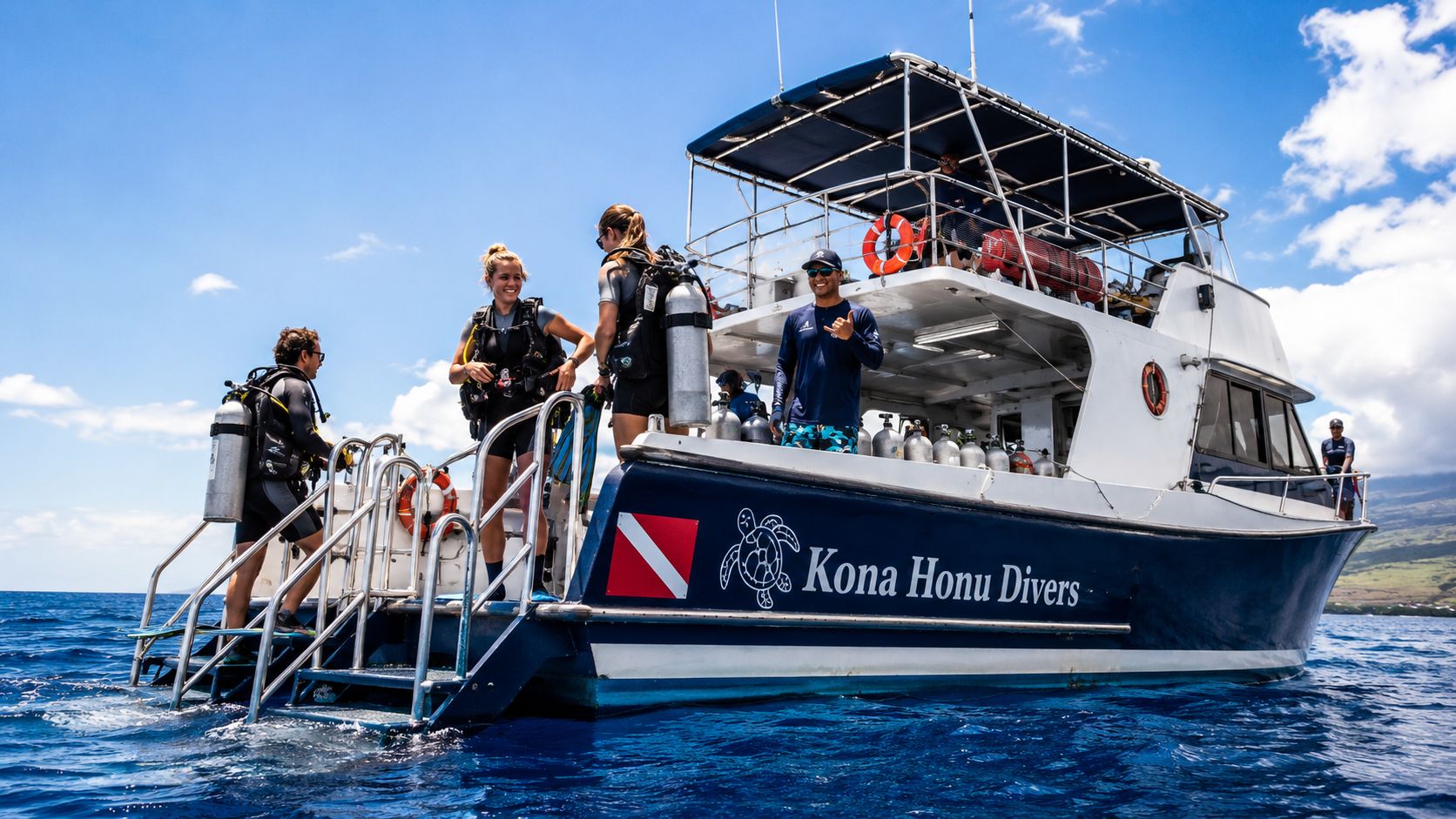 Scuba divers preparing to dive from a Kona Honu Divers boat in the bright blue ocean water.