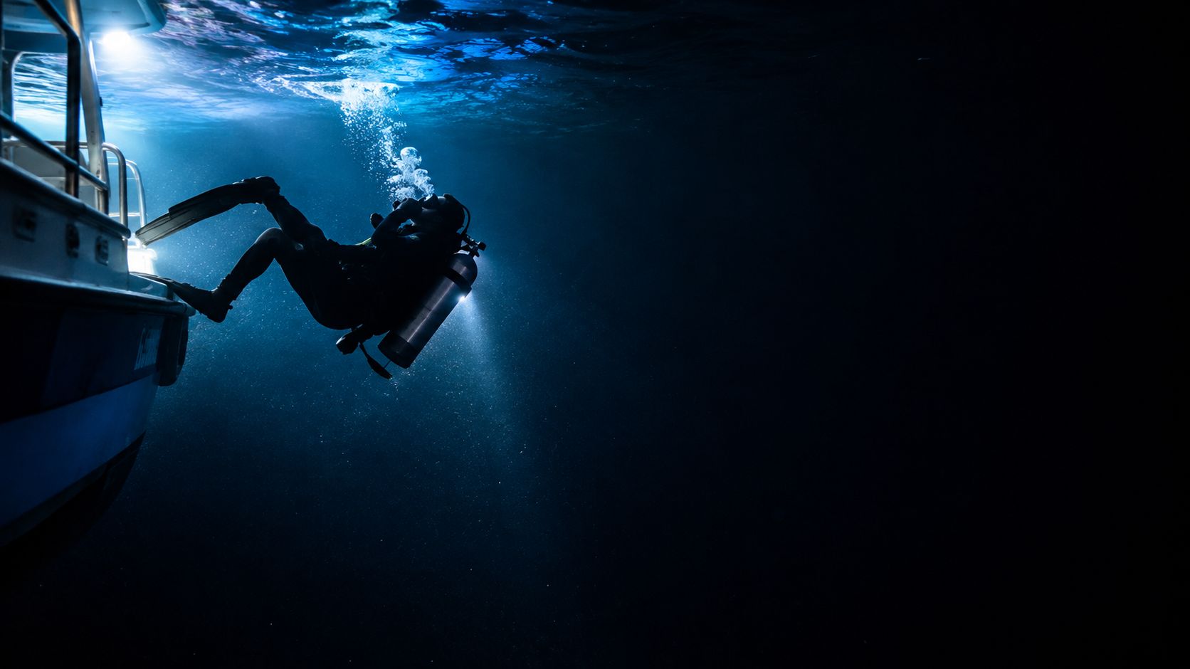 A scuba diver entering the water from a boat during a night dive in dark ocean waters.