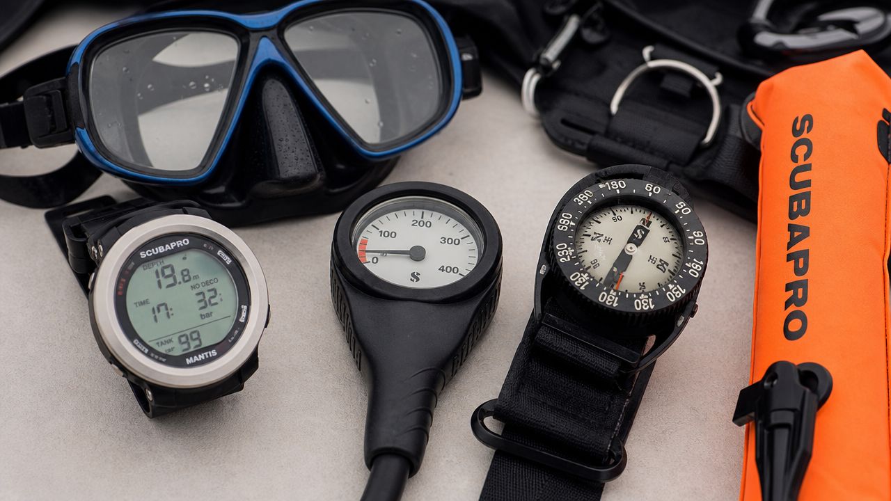 A flat lay of professional scuba diving equipment including a mask, computer, pressure gauge, compass, and buoy.