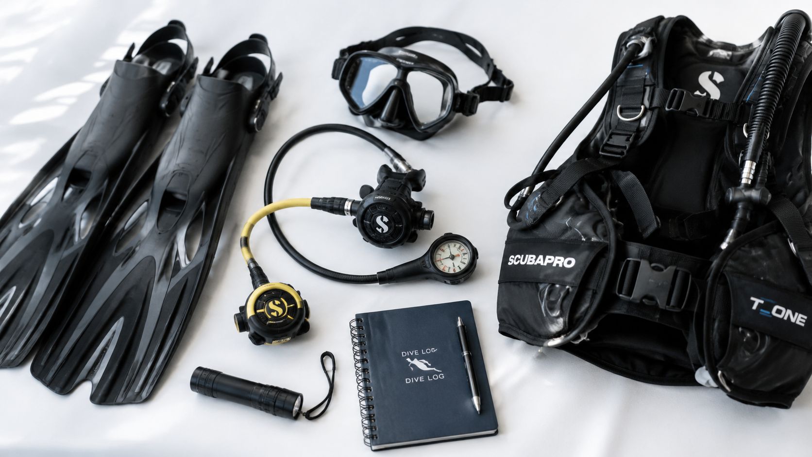 A flat lay of professional scuba diving equipment including fins, a mask, regulator, buoyancy compensator and logbook.