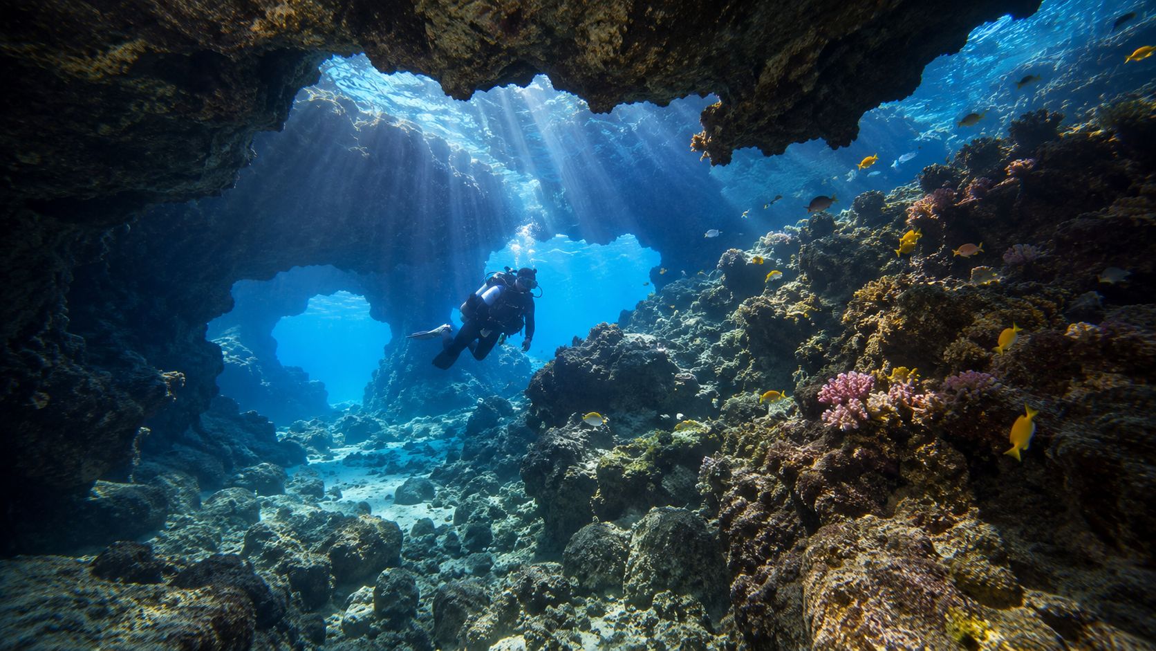 A scuba diver explores a stunning underwater cave system with dramatic sunbeams piercing through the surface water.