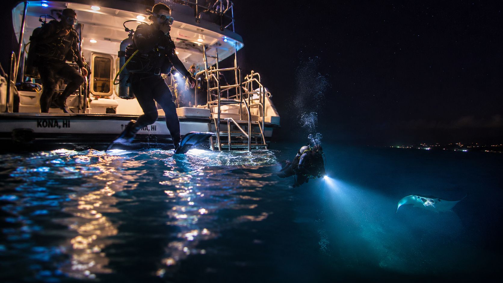 Scuba divers entering the water at night from a boat in Kona to swim with manta rays.