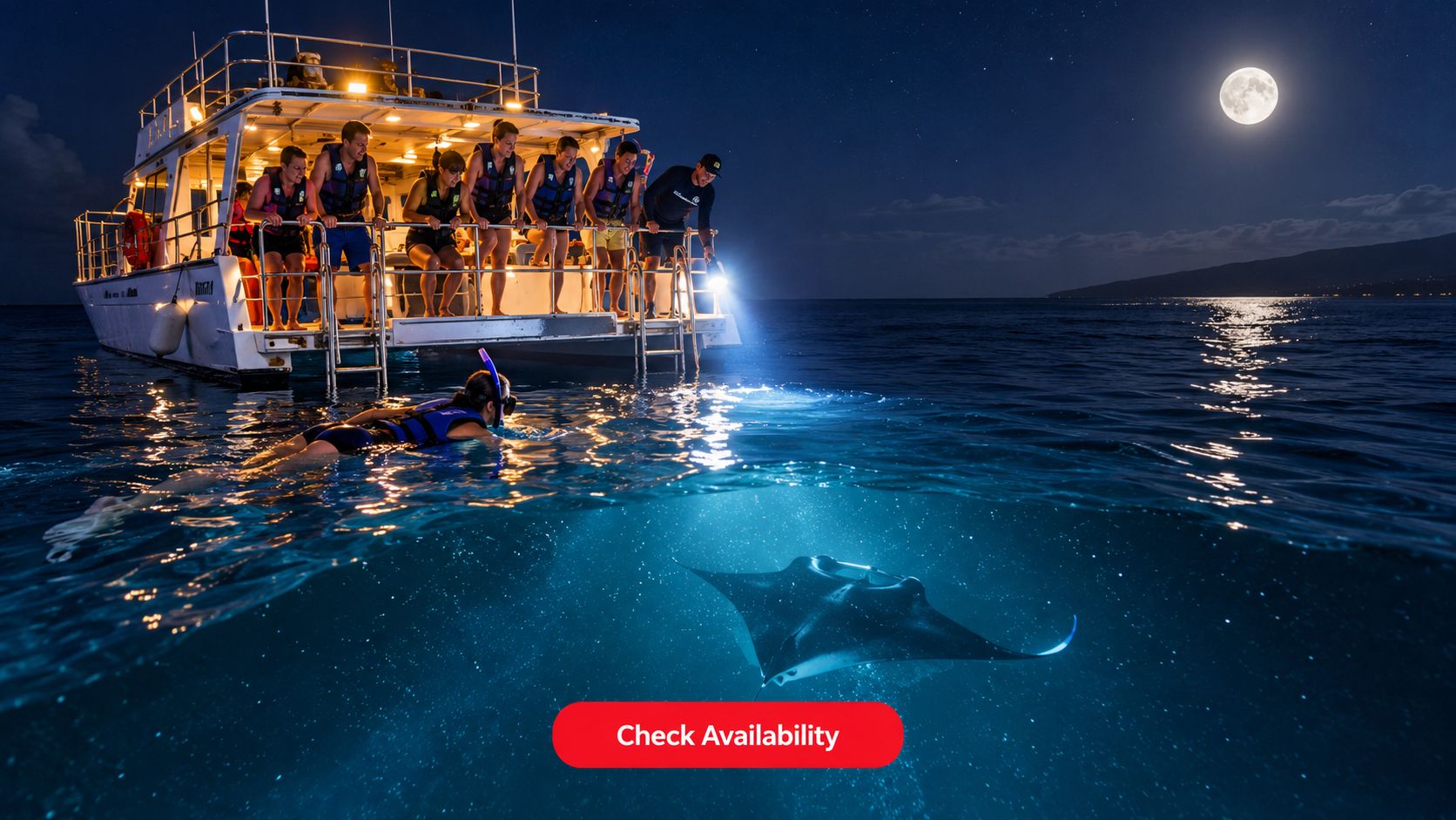A group of snorkelers observe a graceful manta ray swimming under the moonlit water during a night tour.